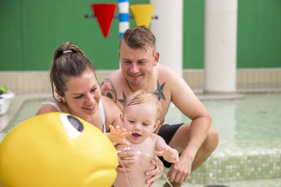 Familie i indend�rs badeland p� feriecenter � pak badet�j og h�ndkl�der klar til flere poolbes�g